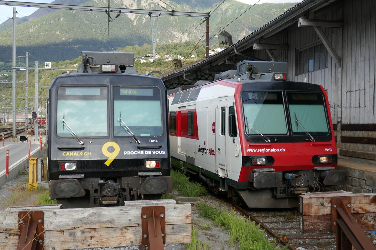 Die RegionAlps Dominos RA14 mit Kanal 9 Vollwerbung und RA12 am 8.8.23 beim Bahnhof Brig abgestellt.