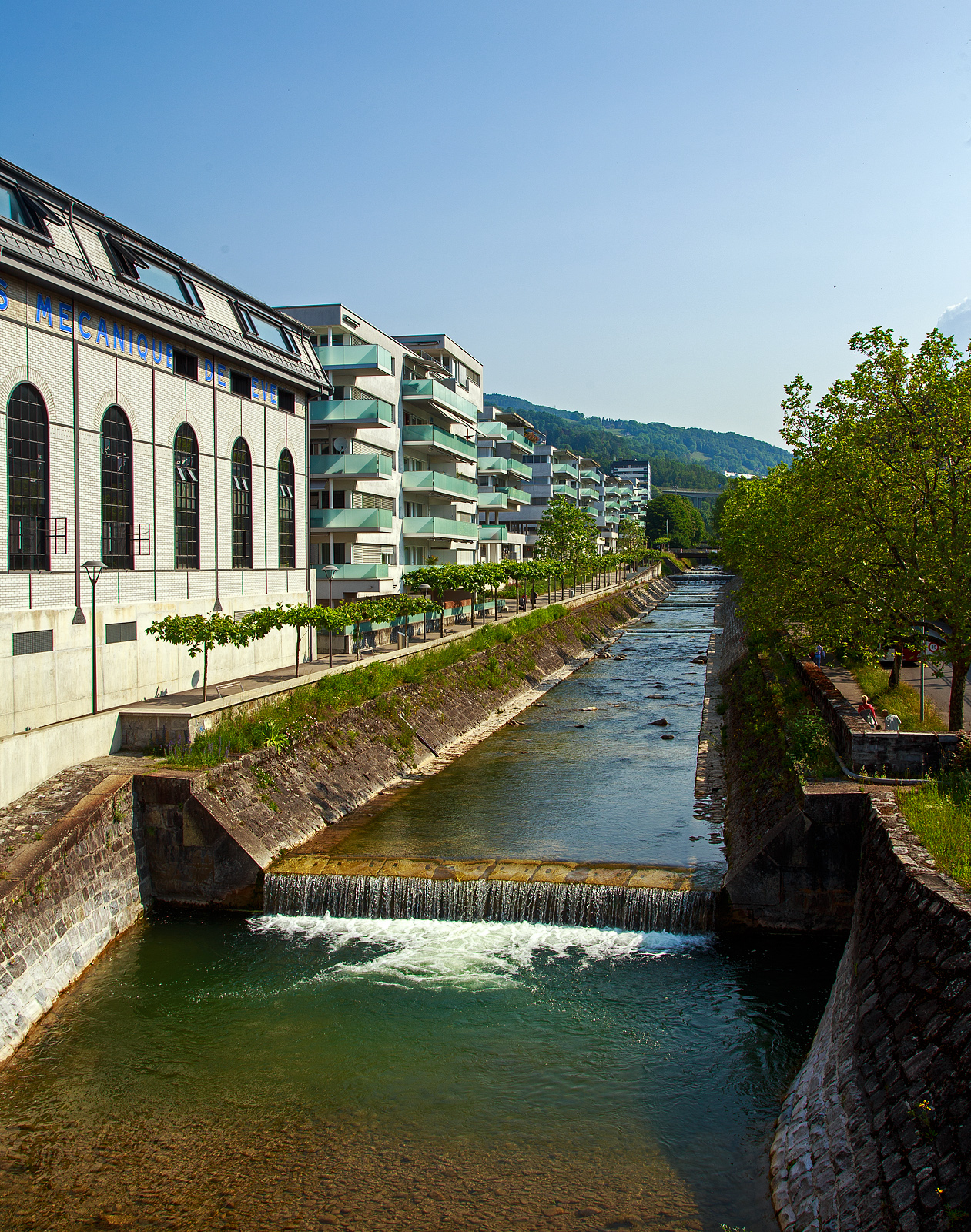 Das Flüsschen Ruisseau de Bergère in Vevey (Waadt) am 28.05.2023, es hat es nicht mehr weit zur Mündung in den Genfersee. 

Die Stadt Vevey am Nordostufer des Genfersees war früher ein bedeutender Handelsplatz und profitierte im 19. Jahrhundert vom Aufschwung durch Industrie und Fremdenverkehr, die noch heute die Hauptsäulen der Wirtschaft darstellen. Bekanntheit erlangte die Stadt auch als Hauptsitz der Nestlé S.A., aber auch links in der ehemaligen Fabrikhalle des 1842 gegründeten Ateliers de constructions mécaniques de Vevey (ACMV) wurden bis 1992 u.a. Schienenfahrzeuge gebaut. Die Herstellung von Eisenbahnwagen konnte in der Fabrik Villeneuve als Vevey Technologies SA weitergeführt werden und wurde 1998 von Bombardier gekauft.
